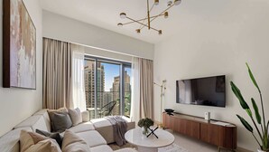 A modern living room with a sectional sofa, a coffee table, a TV, and a large window with curtains. - Silkhaus Luxurious 1BR Downtown Burj Royale (Dubai)