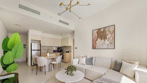 A modern living room with a sectional sofa, a dining area, and a kitchen in the background. - Silkhaus Luxurious 1BR Downtown Burj Royale (Dubai)
