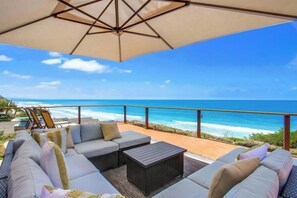 A beachside patio with a sofa set, a table, and an umbrella. - Moonlight Seaside Retreat | Oceanfront Living in Encinitas (Encinitas)