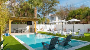 Ein Garten mit Swimmingpool, Liegestühlen, einer Pergola und einer Terrasse mit Sonnenschirmen.