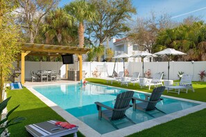A backyard with a swimming pool, lounge chairs, a pergola, and a patio area with umbrellas.