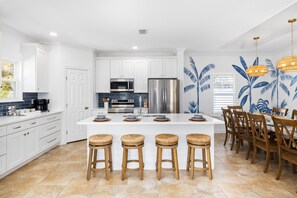 A modern kitchen with white cabinetry, a central island with stools, stainless steel appliances, and a dining area with wooden chairs.