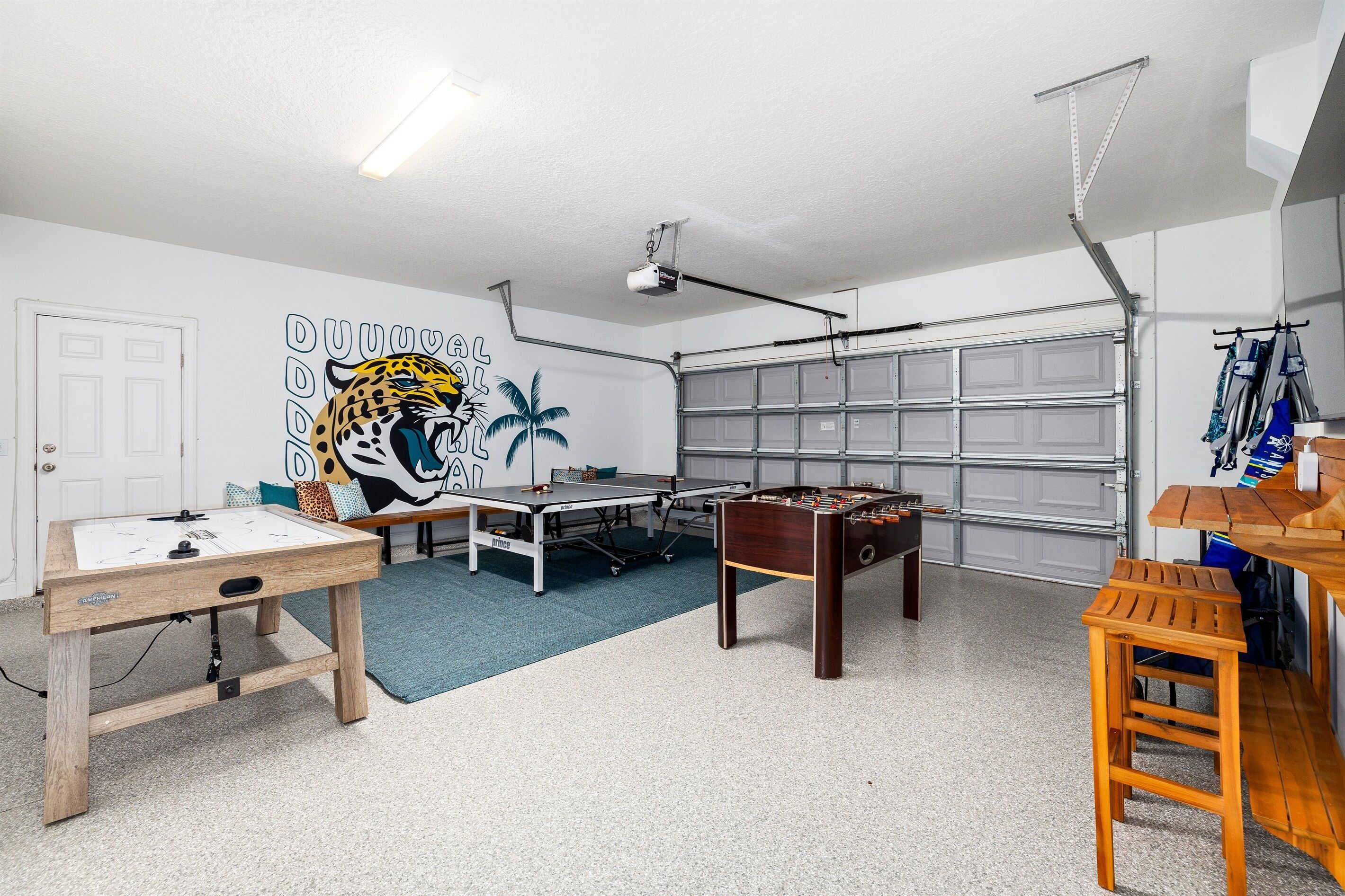 Ein Raum mit einem Kicker, einem Tischtennistisch und einer Wandmalerei eines Jaguars.