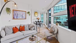 A modern living room with a sofa, coffee table, and a large window with a view of the city. - Luxury Cube Penthouse 2BR 2BA, City Center (Birmingham)