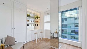 A modern kitchen with white cabinetry, a wooden floor, and a large window with a city view. - Luxury Cube Penthouse 2BR 2BA, City Center (Birmingham)