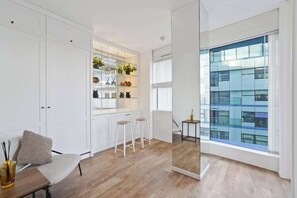 Une cuisine moderne avec des meubles blancs, un plancher en bois et une grande fenêtre donnant sur la ville.