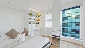 A modern hotel room with a large bed, a glass partition, and a view of a building. - Luxury Cube Penthouse 2BR 2BA, City Center (Birmingham)