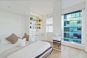 A modern hotel room with a large bed, a glass partition, and a view of a building. - Luxury Cube Penthouse 2BR 2BA, City Center (Birmingham)