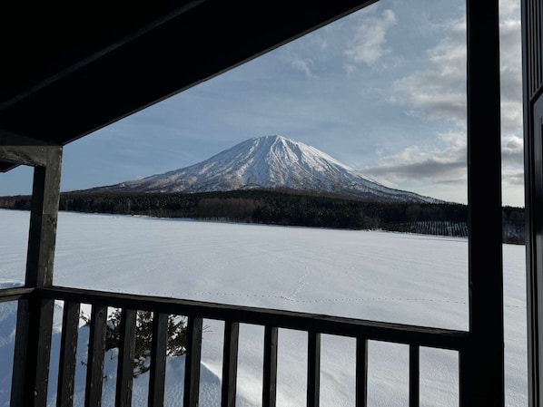 A snow-covered mountain viewed from a covered balcony with a wooden railing.