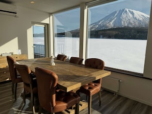 A dining area with a wooden table and leather chairs, large windows with a mountain view, and a radiator on the wall.