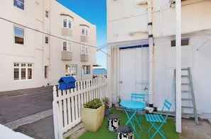 Une petite terrasse extérieure avec une table et des chaises, une clôture blanche en bois et un bâtiment doté de nombreuses fenêtres et de balcons.