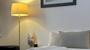 Un lit bien fait, avec une serviette blanche pliée, une lampe de chevet, un tableau encadré au mur et un petit vase avec des fleurs.