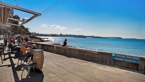 Un espace de restauration situé au bord de l’eau, avec des tables en plein air, une vue sur l’océan et un panneau indiquant « Réserve aquatique de Cabbage Tree Bay ».