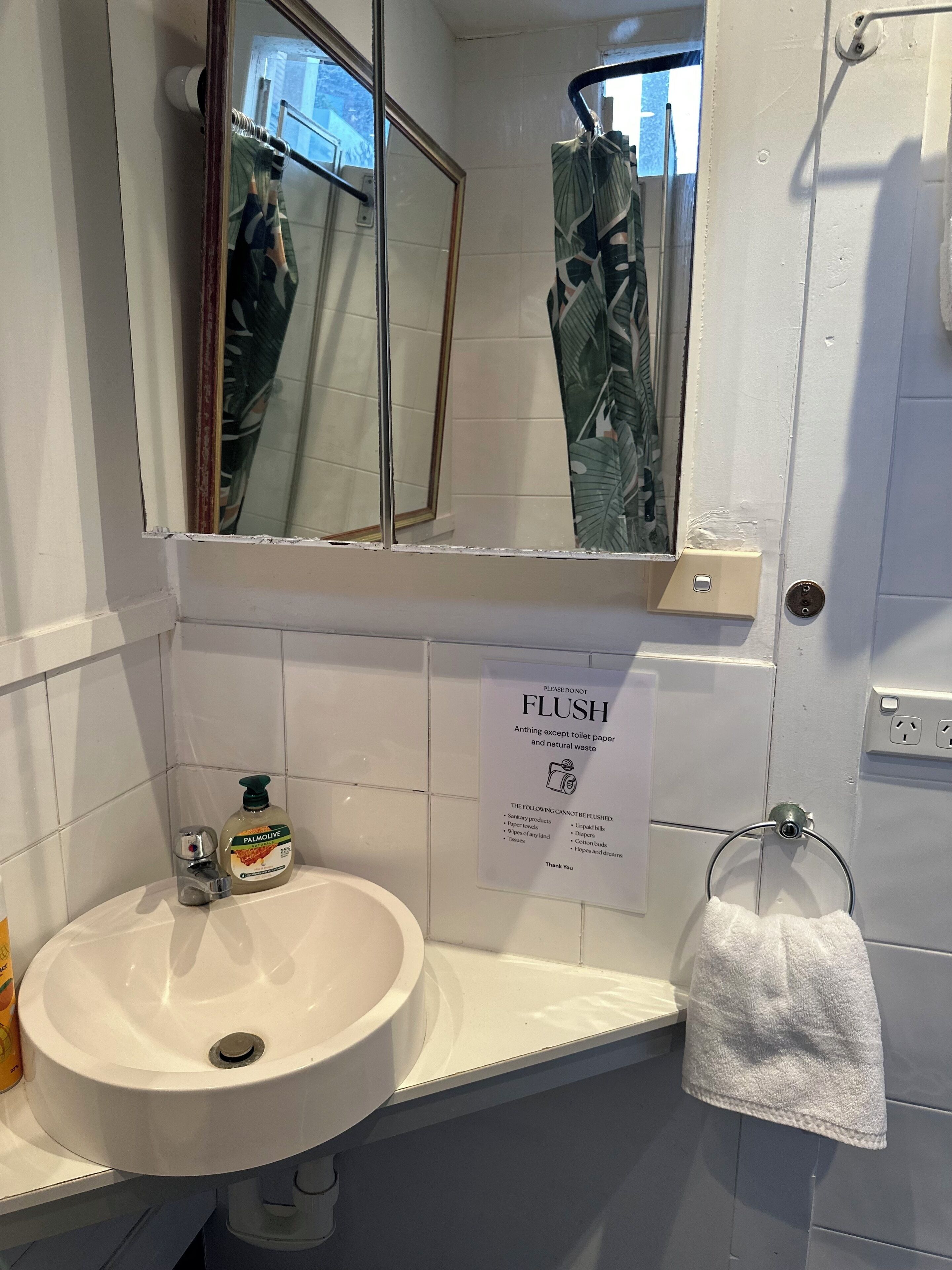 Une salle de bain avec un lavabo blanc, un miroir, un porte-serviettes et un panneau indiquant : « Veuillez ne pas tirer la chasse d’eau ».