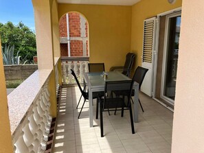 A balcony with a table and chairs, a white balustrade, a glass door, and a brick wall in the background. - 2BR Apartment With Garden in Povljana (Povljana)