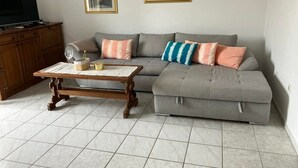 A living room with a grey sectional sofa, a wooden coffee table, and two framed floral paintings on the wall. - 2BR Apartment With Garden in Povljana (Povljana)