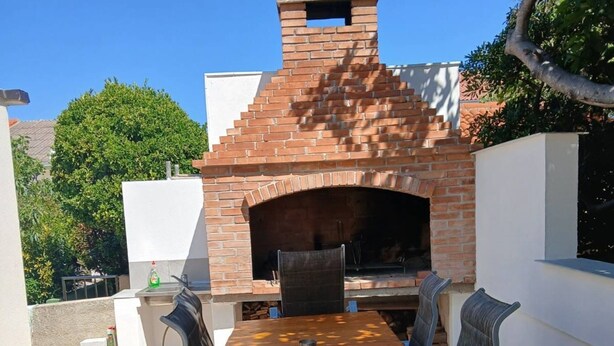 An outdoor brick oven with a table and chairs in a patio area. - 2BR Apartment With Garden in Povljana (Povljana)