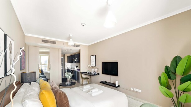 A modern hotel room with a bed, a desk, a TV, and a potted plant. - Silkhaus Modern Studio Near Almas in West Lake (Dubai)