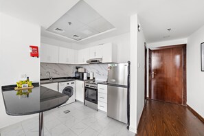 A modern kitchen with white cabinets, a black countertop, stainless steel appliances, and a wooden door. - Silkhaus Lux Studio Binghatti Pearl Near Mall (Dubai)