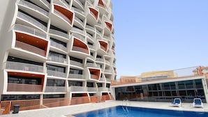 A modern building with multiple balconies, a swimming pool, and a covered area with seating. - Silkhaus Lux Studio Binghatti Pearl Near Mall (Dubai)