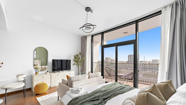 A modern bedroom with a large bed, a television, a sofa, and a balcony with a city view. - Silkhaus Lux Studio Binghatti Pearl Near Mall (Dubai)
