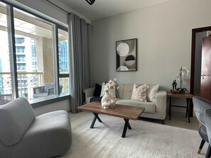 A modern living room with a sofa, a coffee table, and a view of a cityscape through large windows. - Silkhaus Luxury 1BR Emaar Near Burj Khalifa (Dubai)
