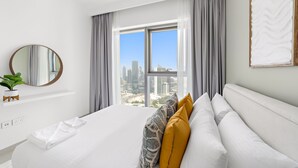 Moderni hotellihuone, jossa on suuri sänky, näköala kaupunkiin ja pyöreä peili seinällä.