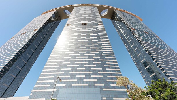 A tall, modern skyscraper with a distinctive curved top and large circular windows. - Silkhaus Gate Tower Luxurious Studio w City View (Abu Dhabi)