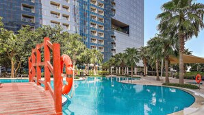 A swimming pool with a lifebuoy, palm trees, and a modern building in the background. - Silkhaus Gate Tower Luxurious Studio w City View (Abu Dhabi)