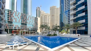 A swimming pool with lounge chairs, surrounded by modern buildings and palm trees. - Silkhaus Dubai Marina Studio Bay Central Tower (Dubai)