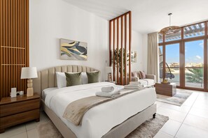 A modern bedroom with a large bed, a nightstand, a bedside table, a lamp, a painting, a plant, and a view of the outdoors through large windows. - Silkhaus Cozy Seashore Studio in Palm Jumeirah (Dubai)