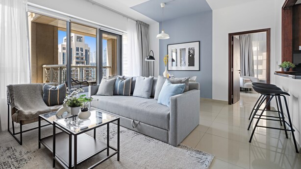 A modern living room with a grey sofa, a glass coffee table, and a bar stool. - Silkhaus Modern 1BR 29 Blvd Heart of Downtown (Dubai)