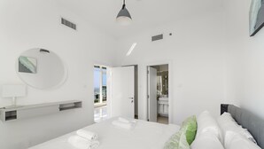 Una habitación de hotel moderna con una cama grande, un espejo redondo, una mesita de noche y vistas al balcón.