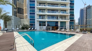 Un hotel moderno con piscina en la azotea, varios balcones y vistas a edificios altos circundantes.