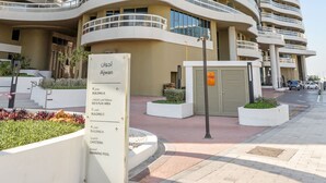 Ein modernes, mehrgeschossiges Hotel mit einer geschwungenen Fassade, einer Schilderung mit angebotenen Annehmlichkeiten wie einem Schwimmbad und einer begrünten Anlage mit Pflanzen.