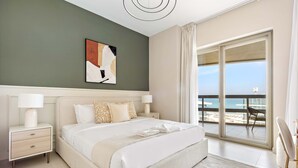 Ein modernes Hotelzimmer mit einem großen Bett, einem Nachttisch, Blick auf den Strand und einem Balkon mit einem Stuhl.
