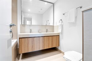 Un baño moderno con un tocador de madera, un espejo grande y un inodoro blanco.
