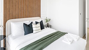 A neatly made bed with white bedding and a green throw, a bedside table with a vase, and a wooden panel wall. - Silkhaus Stylish 2BR Downtown Views II Emaar (Dubai)