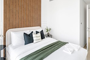 A neatly made bed with white bedding and a green throw, a bedside table with a vase, and a wooden panel wall. - Silkhaus Stylish 2BR Downtown Views II Emaar (Dubai)