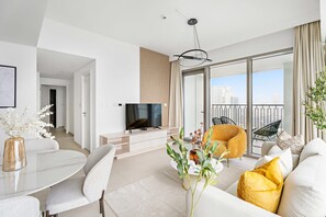 A modern living room with a flat-screen TV, a dining area with a white table and chairs, a sofa with yellow cushions, and a balcony with a view of the city. - Silkhaus Stylish 2BR Downtown Views II Emaar (Dubai)