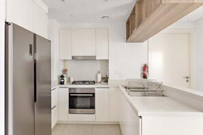 A modern kitchen with white cabinetry, a stainless steel refrigerator, a built-in oven, and a gas stove. - Silkhaus Big 2BR Downtown Views II Emaar Tower (Dubai)