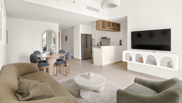 A modern living room with a sofa, chairs, a coffee table, a TV, and a kitchen area in the background. - Silkhaus Big 2BR Downtown Views II Emaar Tower (Dubai)
