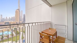 A balcony with a wooden table and chairs, offering a view of the cityscape and a swimming pool. - Silkhaus Big 2BR Downtown Views II Emaar Tower (Dubai)