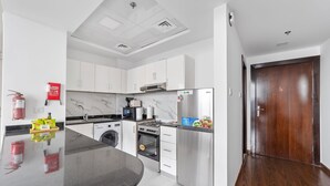 A modern kitchen with white cabinets, a stainless steel refrigerator, a built-in oven, and a microwave. - Silkhaus New Studio Binghatti Pearl in DSO (Dubai)