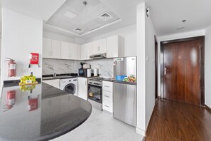 A modern kitchen with white cabinets, a stainless steel refrigerator, a built-in oven, and a microwave. - Silkhaus New Studio Binghatti Pearl in DSO (Dubai)