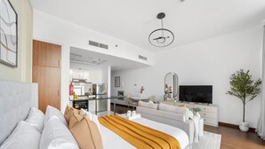 A modern hotel room with a large bed, a TV, a sofa, a dining area, and a plant. - Silkhaus New Studio Binghatti Pearl in DSO (Dubai)