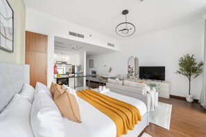 A modern hotel room with a large bed, a TV, a sofa, a dining area, and a plant. - Silkhaus New Studio Binghatti Pearl in DSO (Dubai)