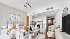 A modern living room with a sofa, a bed, a TV, and a kitchen in the background. - Silkhaus New Studio Binghatti Pearl in DSO (Dubai)