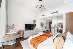 Een moderne hotelkamer met een bed, een bureau, een stoel, een televisie en een kitchenette op de achtergrond.
