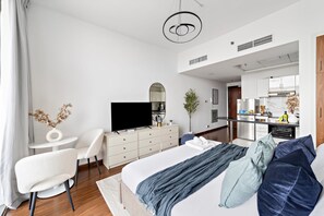 A modern hotel room with a large bed, a television, a dining area, and a kitchenette. - Silkhaus Studio in Silicon Oasis City View (Dubai)